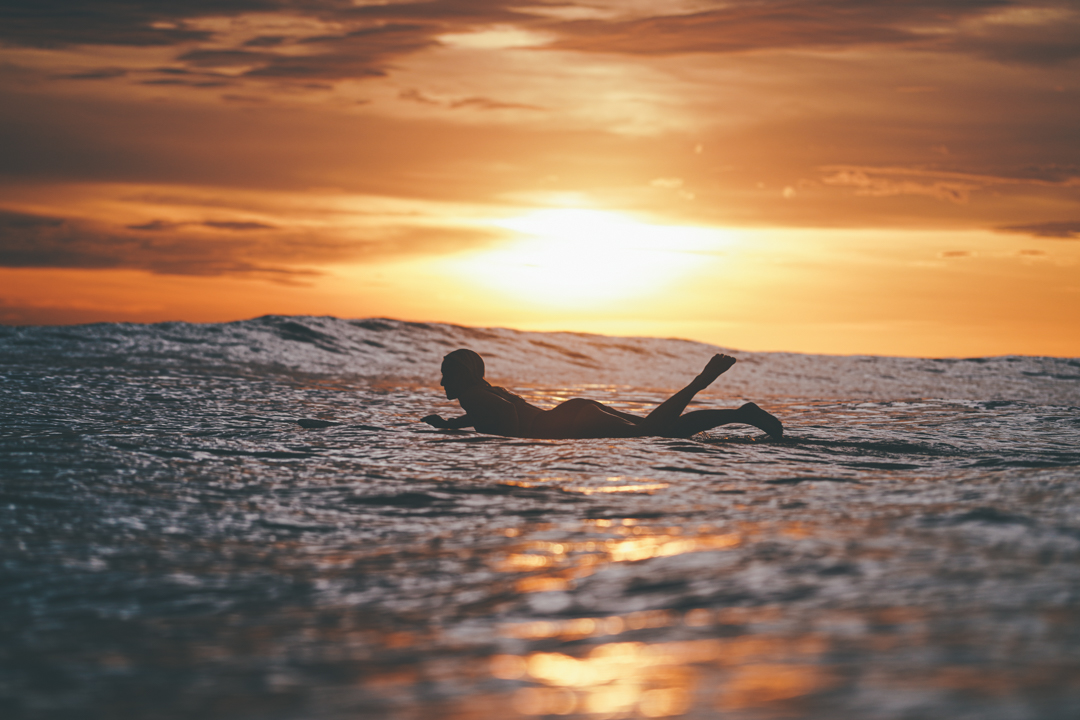 Surfer paddling on calm sea at sunset in Nosara, Guanacaste, with golden sky and waves